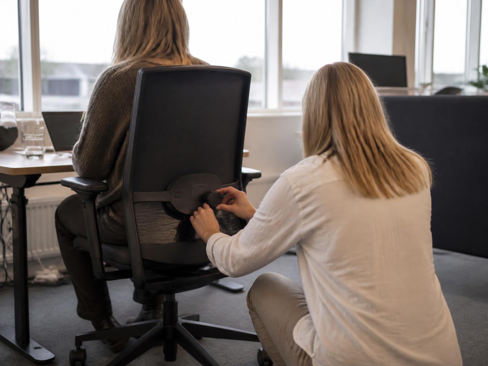 Ergonomikonsulent tilpasser ryglænet på en kontorstol til en siddende medarbejder