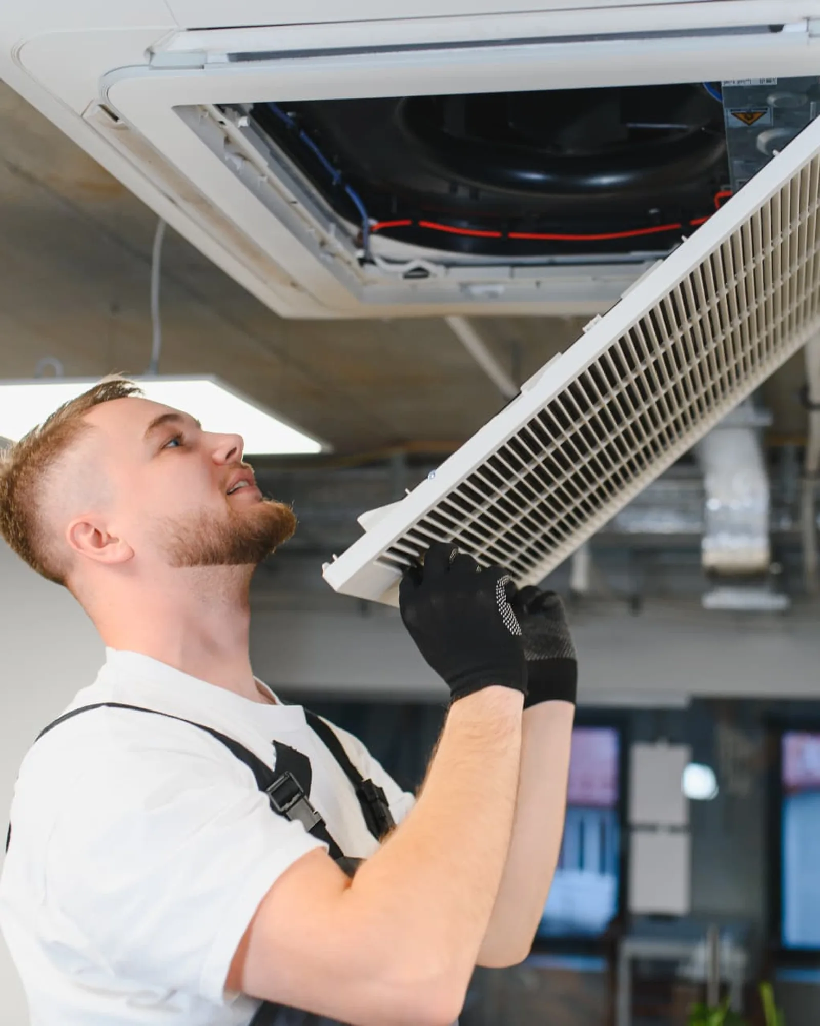Tekniker som utfører service på et ventilasjonsanlegg i taket på en arbeidsplass