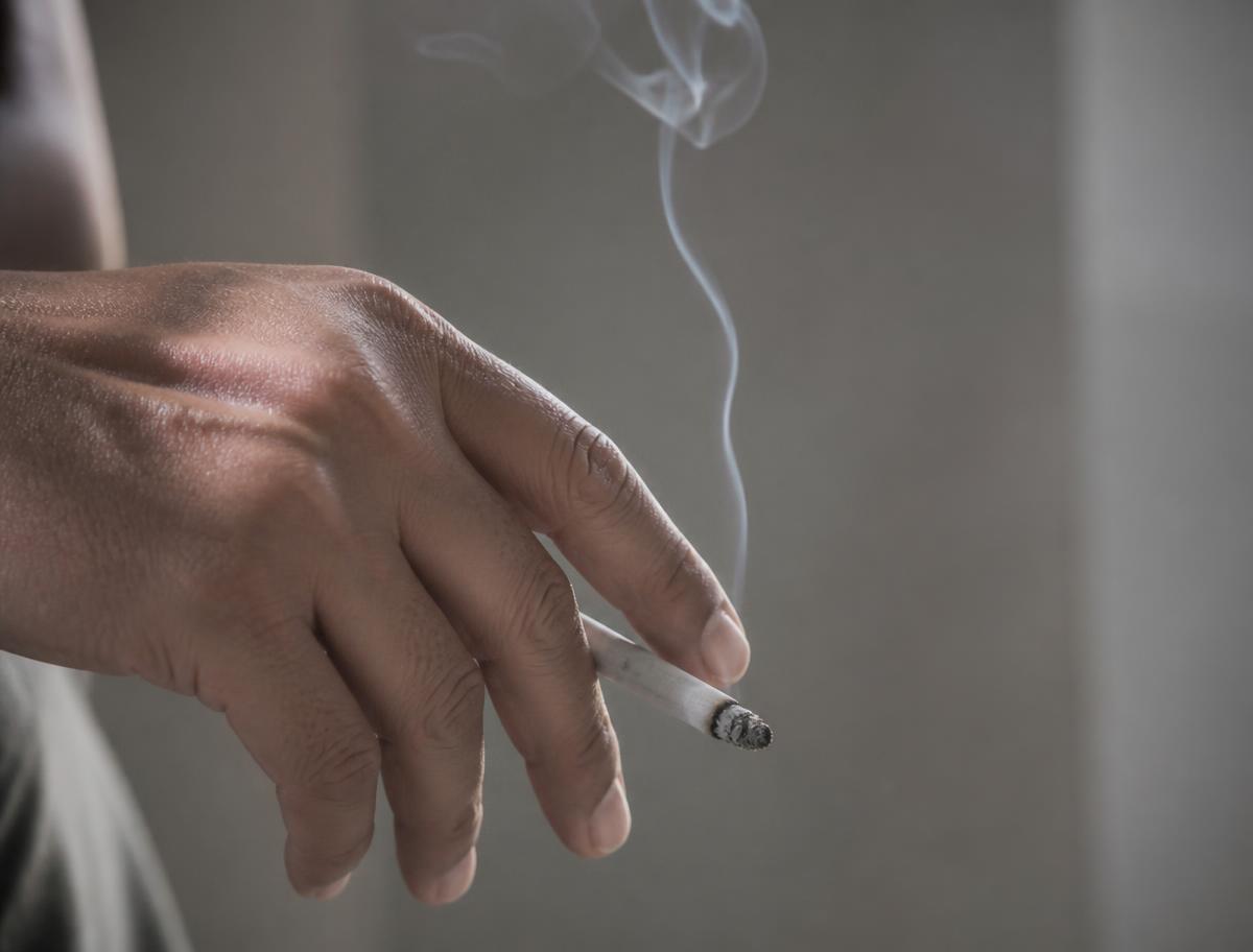 Hånd med tændt cigaret og opstigende røg