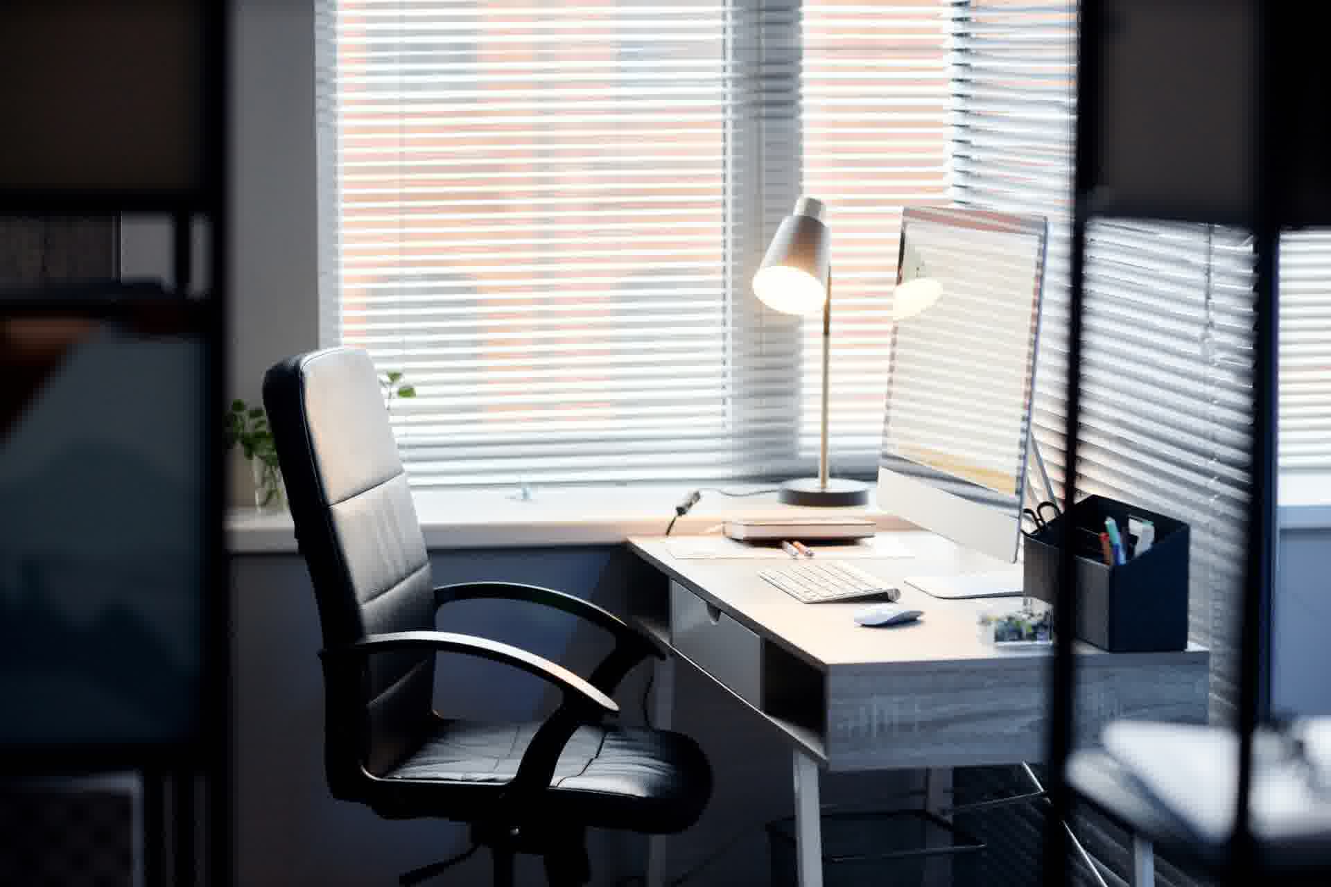 Hjemmekontor ved vindue med kontorstol, skrivebord, skærm og arbejdslampe